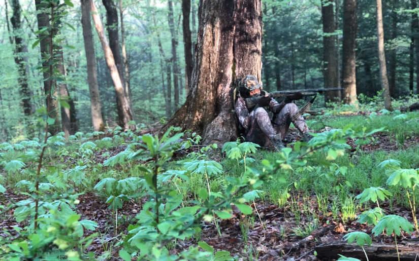 Campfire Collective Hunting Ambassador Danielle Lynise sitting against a tree aiming her shotgun on a hunt.