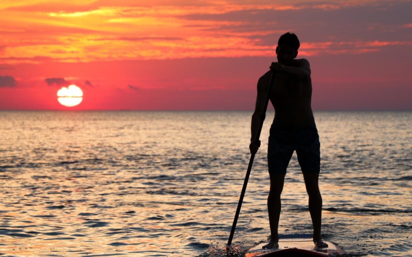 Silhouette of male stand-up paddleboarder at sunset.